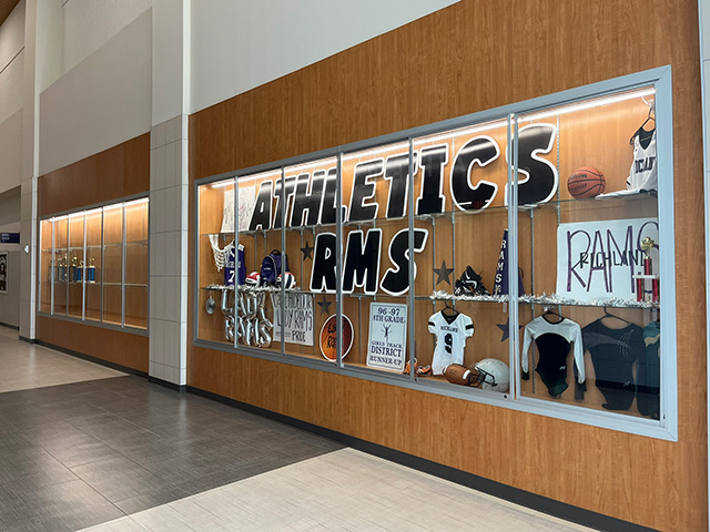 Glass display cases with "ATHLETICS RMS" signage and team sports memorabilia